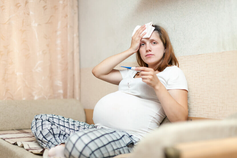 Mulher grávida com termômetro sentada em sala de estar
